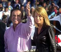 Eks-president Carlos Menem og kona Cecilia Bolocco vinker til tilhengere under et valgarrangement på en fotballstadion i La Matanza, nær Buenos Aires 14. september 2002. (Foto: AP/Daniel Luna)