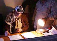 Palestinernes president Yasir Arafat signerer papirer i lyset fra en lommelykt. (Foto: Scanpix/Reuters/Hussein Hussein