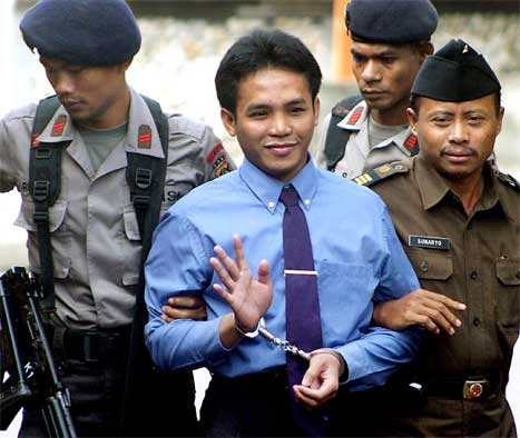 Imron Ali vinker til de frammøtte mens han blir ført inn i rettssalen av to politimenn. (AFP-foto)