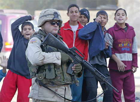 Irakiske barn samler seg rundt en amerikansk soldat som holder vakt etter en bombeeksplosjon i Bagdad i formiddag. (Foto: Reuters-Scanpix)