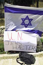 Gjemt bak et israelsk flagg holder en Kach-aktivist opp et banner under en demonstrasjon mot FN i Jerusalem (Scanpix/AP) Gjemt bak et israelsk flagg holder en Kach-aktivist opp et banner under en demonstrasjon mot FN i Jerusalem (Scanpix/AP)