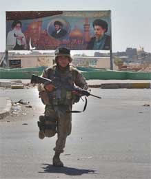 En amerikansk soldat løper forbi en plakat med bilde av Muqtada al-Sadr og hans far i den beleirede byen Najaf (Scanpix/AP)