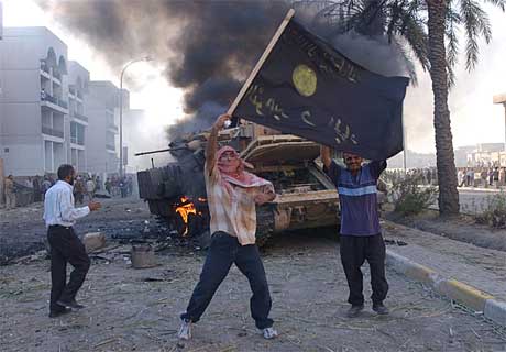 Tilhengere av Abu Musab al-Zarqawi vifter med et flagg ved et ødelagt amerikansk militærkjøretøy. (Arkivfoto: AP/Scanpix)
