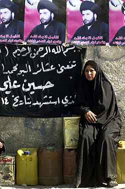 En kvinne sitter under et portrett av sjialederen Moqtada al-Sadr i Sadr-byen i Bagdad. Foto: Karim Kadim, AP 