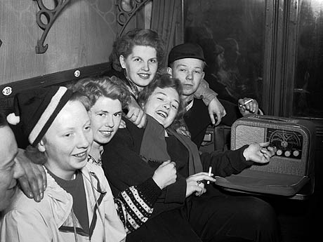 En glad ungdomsgjeng ombord i en røykekupe på Bergenstoget like før avgang fra Østbanen i 1952. En Kurér reiseradio og en sigarett hører med til kosen. Foto: NTB / Scanpix 