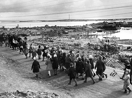 17. mai 1945 feires med barnetog i Vadsø. Ruiner av ødelagte bygninger i bakgrunnen. Foto: NTB / Scanpix 