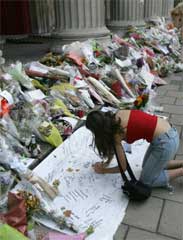 En kvinne skriver sin siste hilsen ved blomstene lagt ned til minne om ofrene i London-bombene. (Foto: Scanpix/AP/R. De La Mauviniere