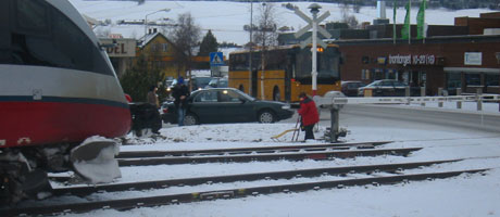 Ei kvinne prøver å komme forbi bommen og ut av jernbanesporet, idet toget passerer. Foto: Joar Elgåen/NRK